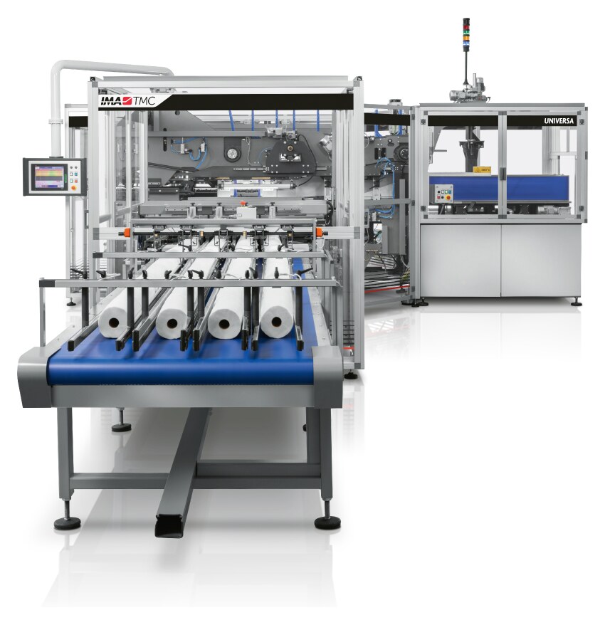 IMA TMC Universa tissue packaging line, kitchen towel rolls riding the blue infeed belt into the wrapper, with the bundler behind it carrying the UNIVERSA badge