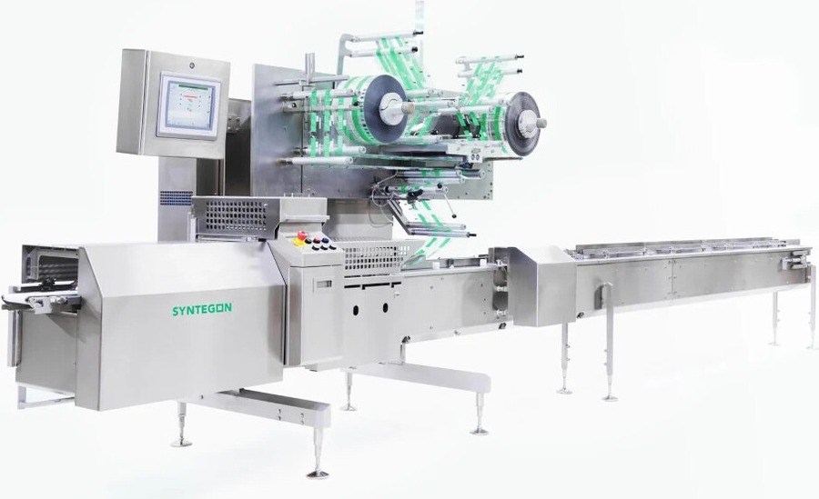 Syntegon Pack 403 HE horizontal flow wrapper with the film reels and crimp jaw section above the infeed and discharge conveyors